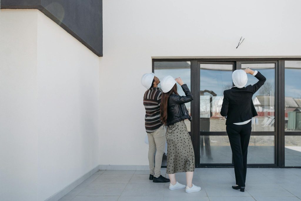 Three architects evaluating exterior building structure, wearing helmets and business attire.